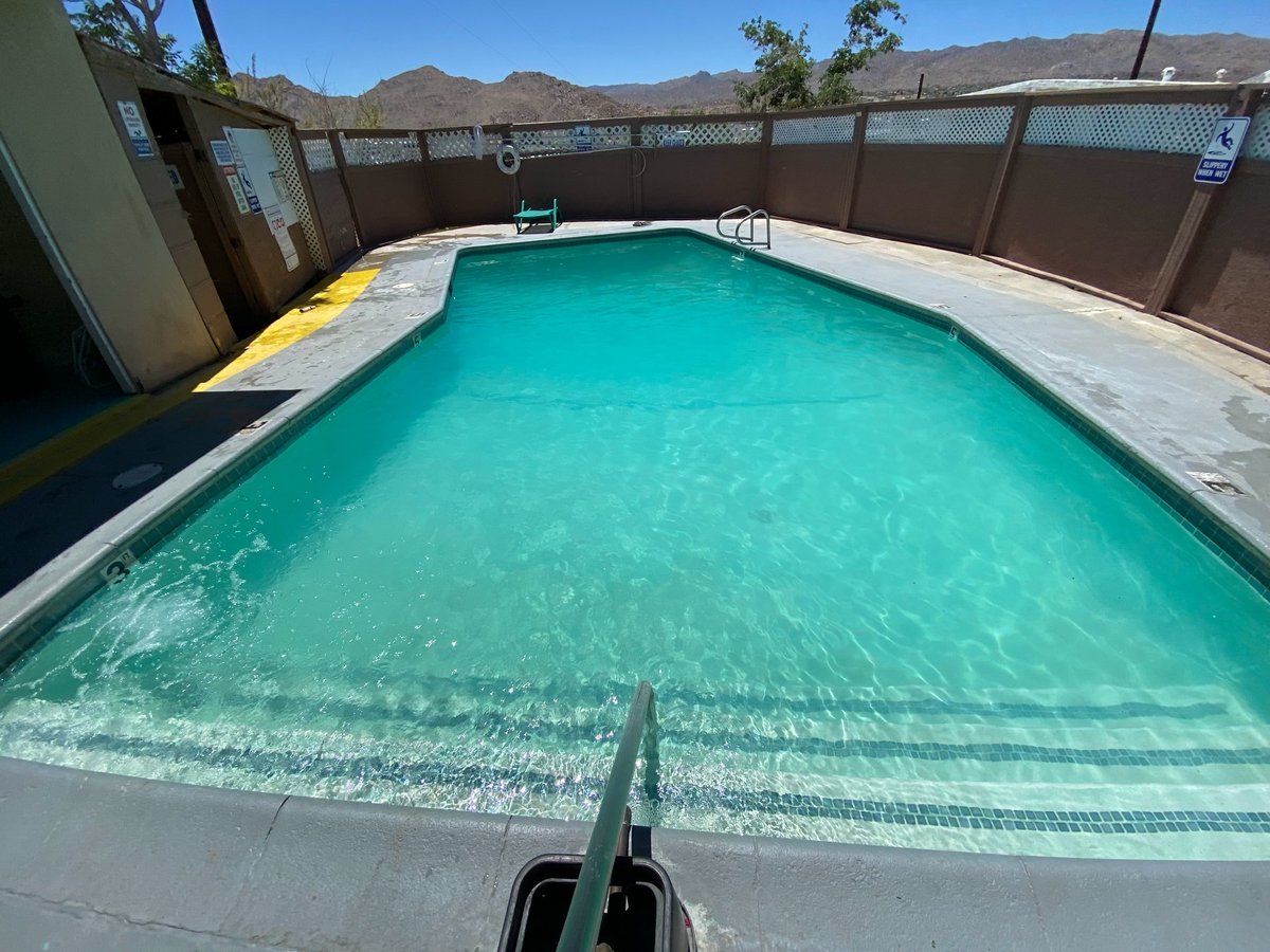 Backyard swimming pool with turquoise water surrounded by concrete deck and brown fence, with desert hills visible in background